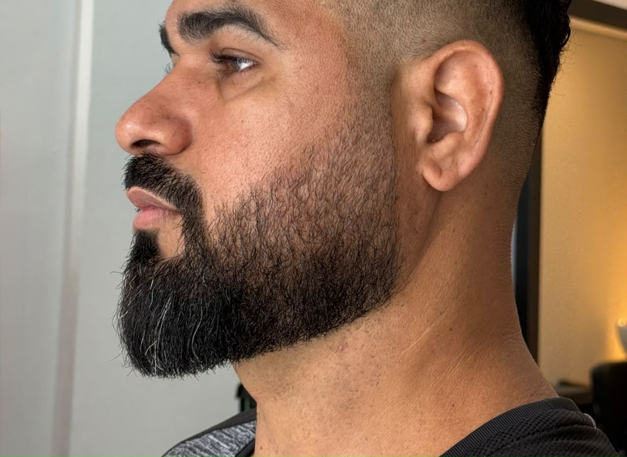 Cliente de perfil com barba desenhada e degradê feitos na Fícus
