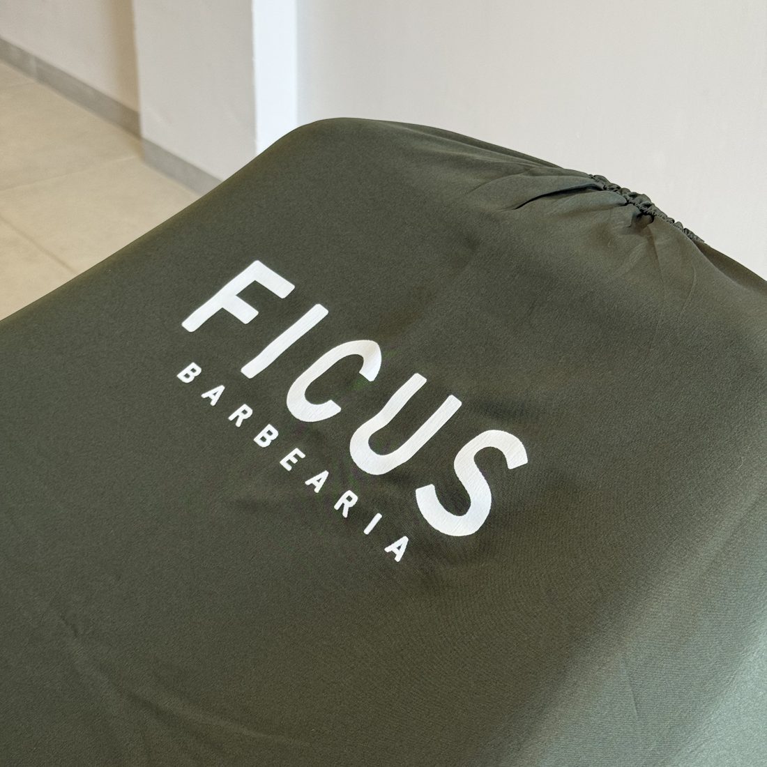 Capa de corte verde-oliva com a marca Ficus Barbearia